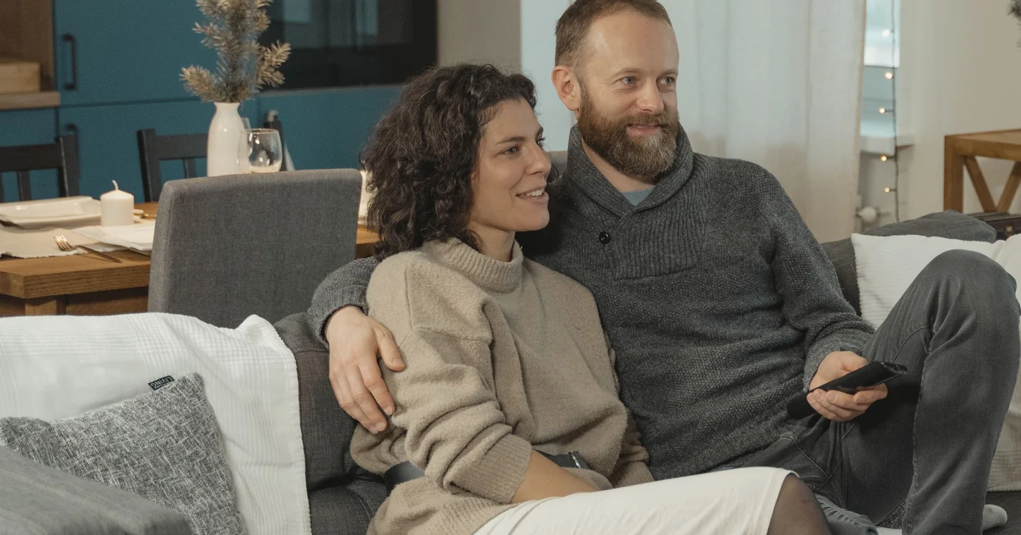 זוג יושב חבוק על הספה בסלון בערב רגיל בבית - לשמר אהבה מתחיל ברגעים הקטנים